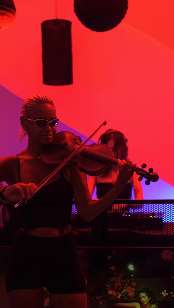 A violinist performing live under deep red and violet light